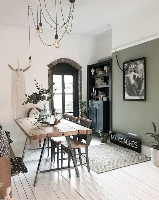 an eclectic dining room with an olive green accent wall, a stained table and metal and wood chairs, hanging bulbs, a built-in sideboard