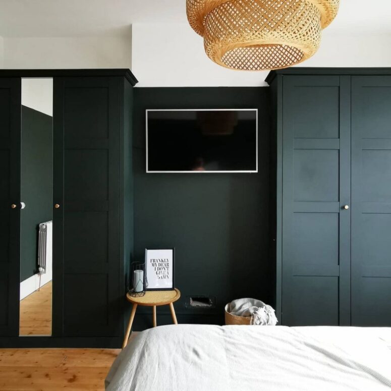 a stylish modern bedroom with black walls and matching black IKEA Pax wardrobes, a mirror, a stool and a TV, a pendant lamp
