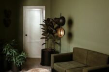 34 an olive green living room wiht a dark green sofa, potted plants, some lovely lamps, a striped rug and a wicker pouf