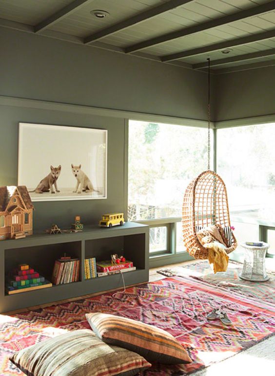 an olive green living room with a matching ceiling and matching shelves, a bold rug and pillows, a pendant egg chair and some toys
