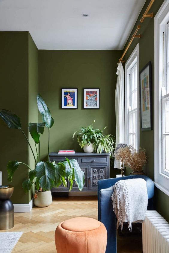 an olive green space with an inlay sideboard, a blue chair and an orange pouf, some bright decor and potted plants is cool