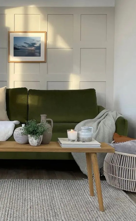 a Scandinavian living room with creamy paneling, an olive green sofa and neutral textiles, a wooden bench with decor