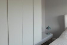 54 a neutral bedroom with IKEA Pax wardrobes raised on a platform, a neutral bed with neutral bedding and a green lamp