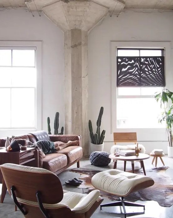 a Scandi inspired living room with a tan leather sofa, a creamy Eames lounger and an ottoman, a coffee table and a cowhide rug