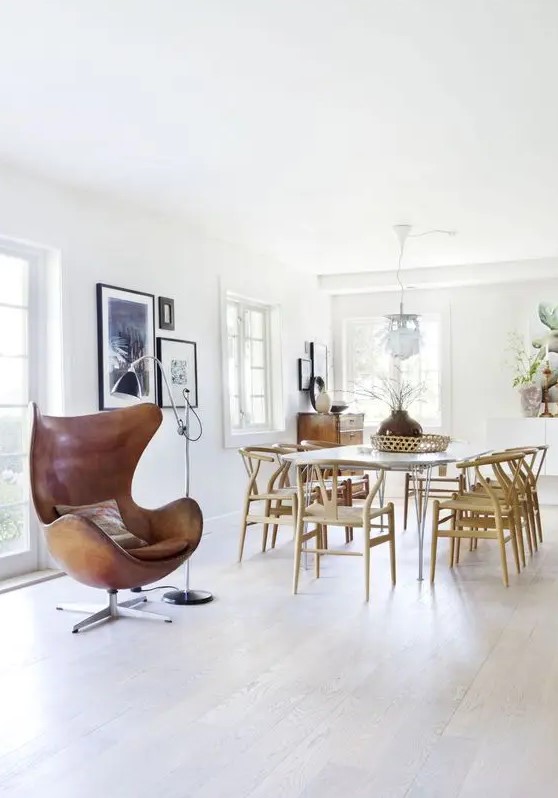 a Scandinavian dining space with a hairpin leg table and Wishbone chairs, a brown leather Egg chair, a floor lamp and some art