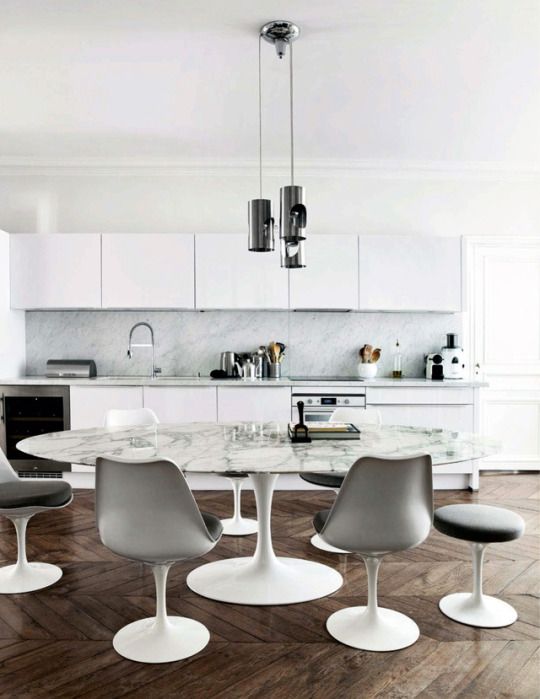 a Scandinavian kitchen in white, with an eating zone with an oval table and grey Tulip chairs