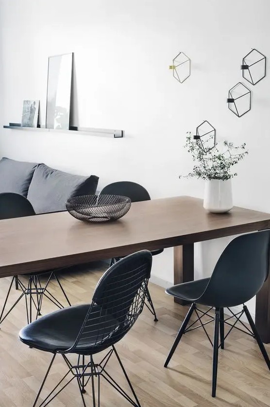 a Scandinavian living and dining room with a grey sofa, a stained table, black Eames and Eames wire chairs and geometric sconces