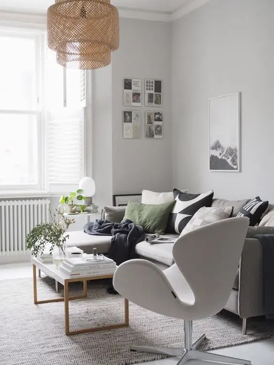 a Scandinavian living room with a grey sofa and printed pillows, a neutral Swan chair, a coffee table, artwork and a woven pendant lamp
