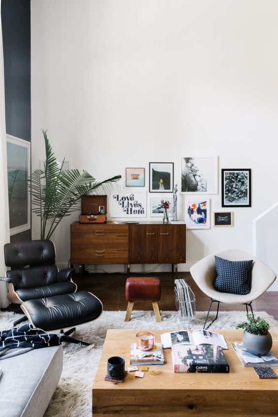 a Scandinavian living room with a stained credenza, a black Eames lounger, some chairs and stools and a coffee table