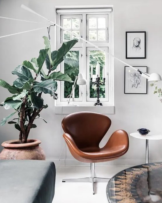 a Scandinavian space with a brown leather Swan chair, a side table, a grey daybed, a coffee table and a potted plant