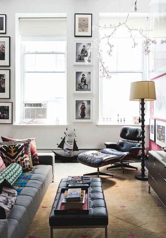 a beautiful living room with gallery walls, a grey sofa, a black Eames lounger, a black ottoman, a TV and a LED branch