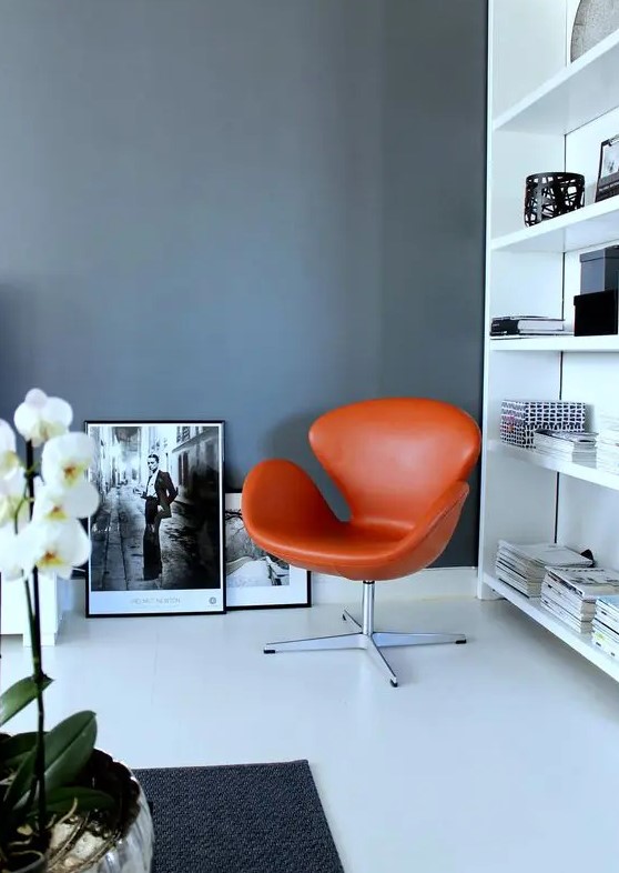 a black and white Scandinavian space with a large bookcase, an orange Swan chair, black and white artwork and a potted plant