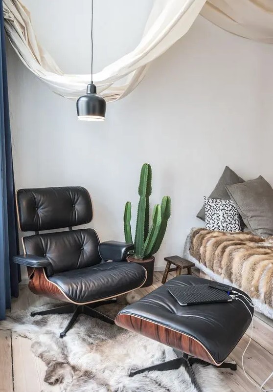 a boho bedroom with a bed with grey pillows and faux fur, a black Eames lounger and an ottoman, a black pendant lamp
