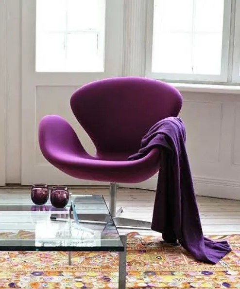 a bold and refined space with a purple Swan chair and a blanket, a coffee table with purpel glasses and a bold rug
