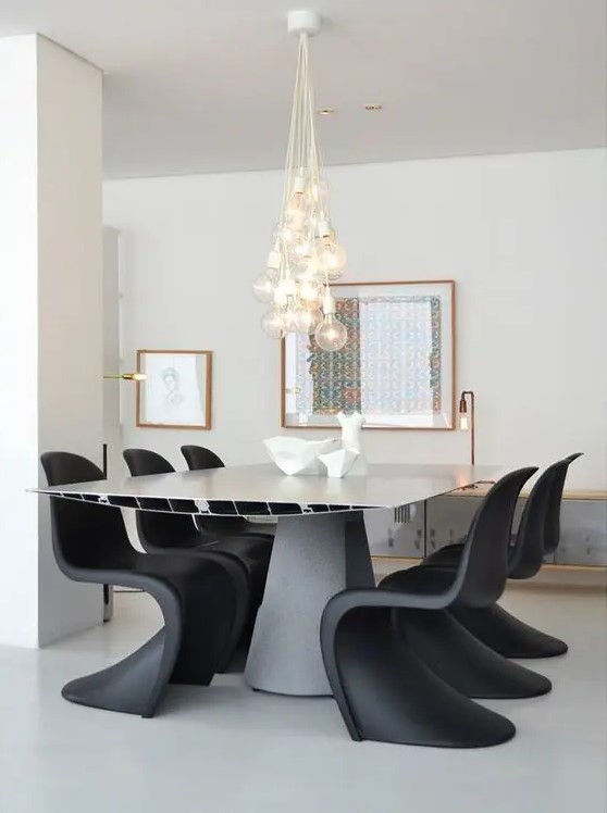 a bold contemporary dining room with a metal dining table, black Panton chairs, a cluster of pendant bulbs and some art