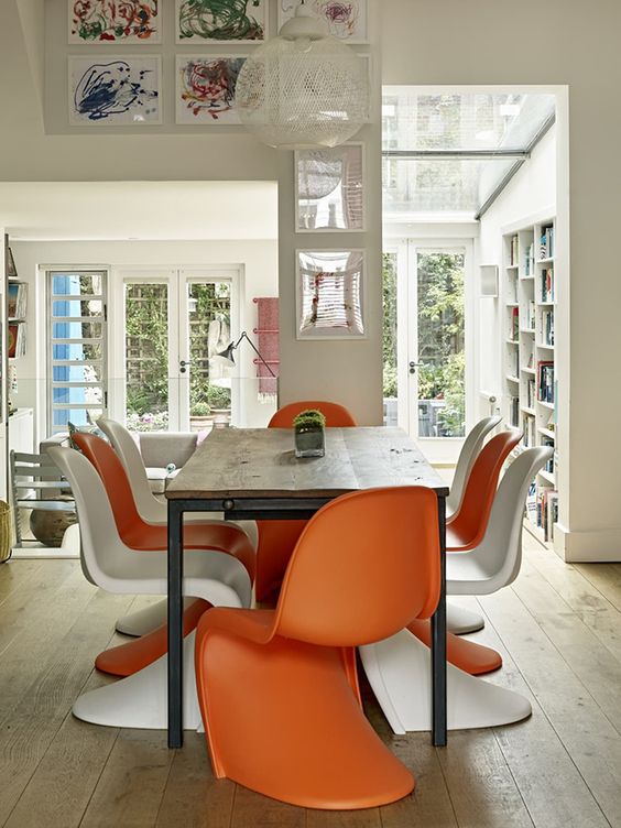 a bold dining room with a stained living edge table, orange and white Panton chairs and some bright artwork