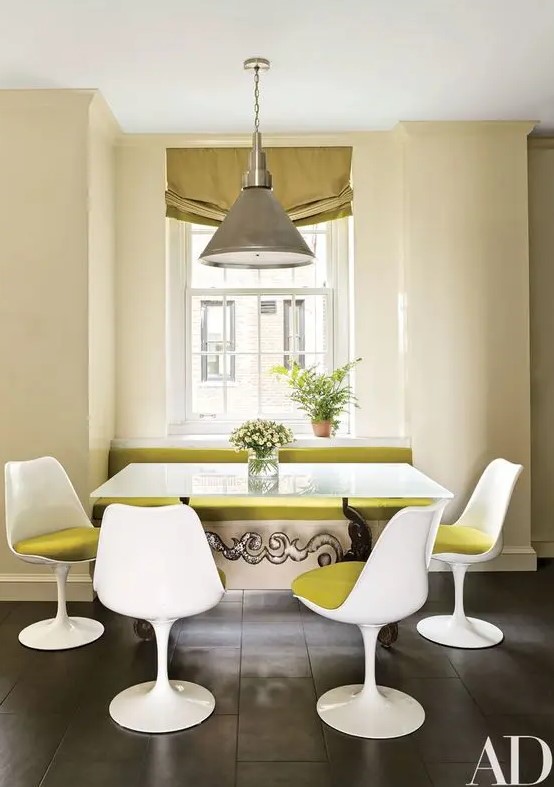 a bold dining space with a windowsill bench with mustard upholstery, a table, and mustard Tulip chairs, a pendant lamp