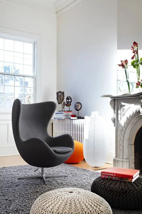 a bold living room with a fireplace and blooms on it, with a grey Egg chair, several knit Poufs and some decor on the radiator