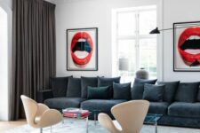 a bold living room with a graphite grey sofa and pillows, glass coffee tables, neutral Swan chairs and bold artwork