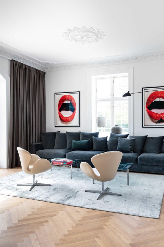 a bold living room with a graphite grey sofa and pillows, glass coffee tables, neutral Swan chairs and bold artwork