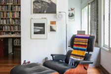 a bold mid-century modern space with a black Eames lounger with a bright blanket, a cowhide rug, a gallery wall