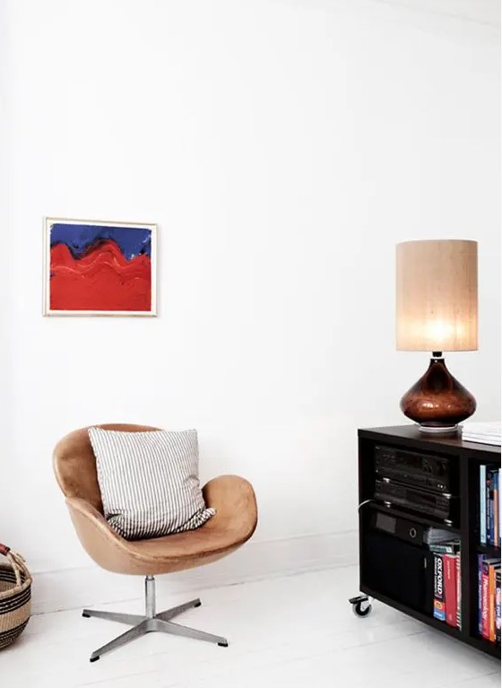 a bold nook with a black storage unit on casters, a table lamp, a tan leather Swan chair and a bold artwork