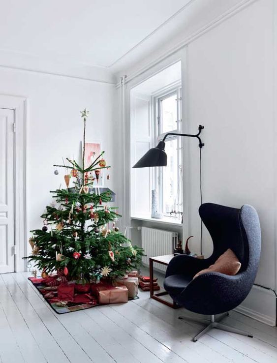 a bright Scandinavian nook with a navy chair, a side table, a Christmas tree with decor and a large black sconce