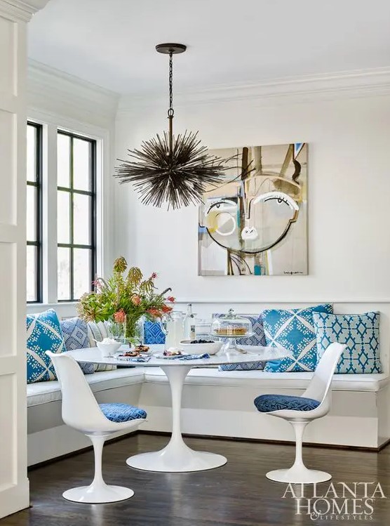 a bright dining space with a corner upholstered bench, a round table and blue Tulip chairs, a black burst chandelier