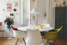 a bright dining space with a round table, Tulip and Eames chairs, a pendant lamp and some colorful home decor