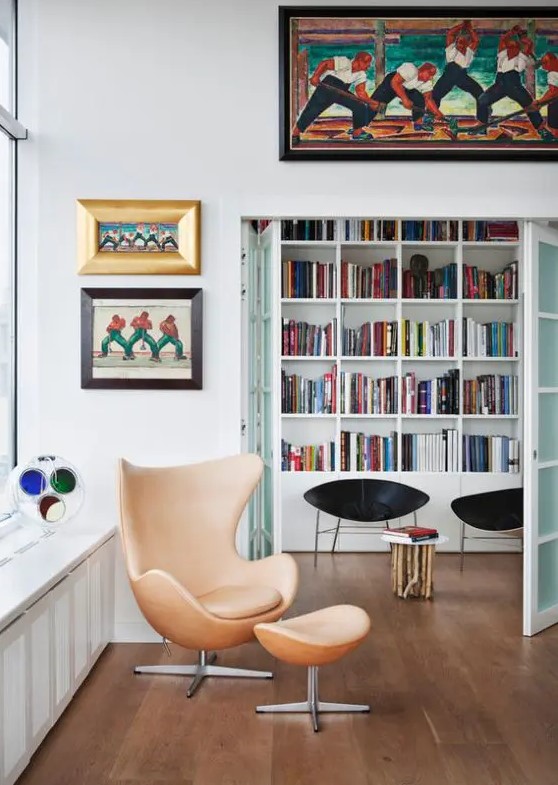 a catchy and bright space with a tan leather Egg chair and a footrest, bold artwork and some black chairs