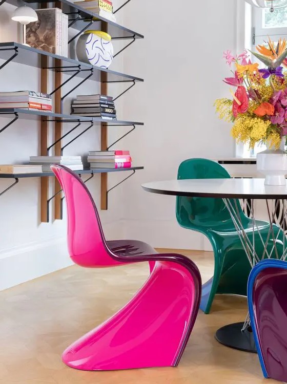 a catchy dining room with wall mounted shelves, a neutral chair and jewel tone Panton chairs plus bold bloos