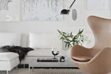 a catchy living room with a creamy corner sofa and pillows, a low coffee table, a gallery wlal and a beige leather Egg chair