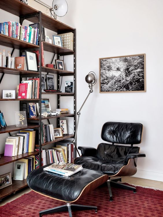 a catchy reading nook with a large industrial bookcase, a black Eames lounger, a bold rug and some industrial lamps