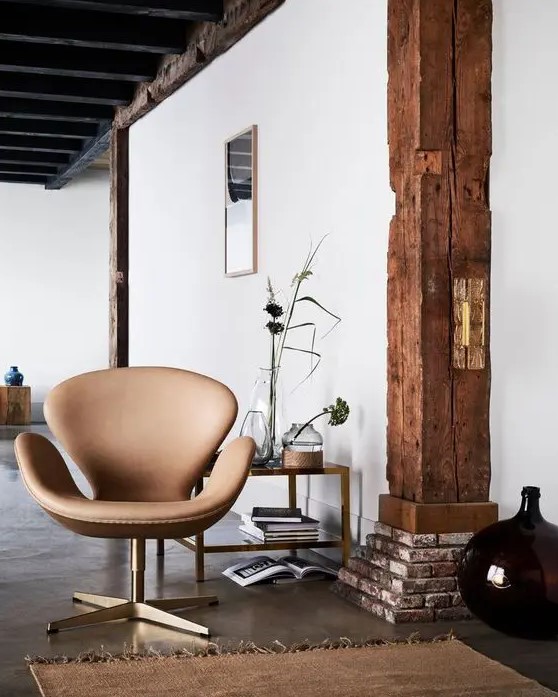 a catchy space with a stained wooden beam, a tan leather Swan chair, a coffee table with decor and a large vase