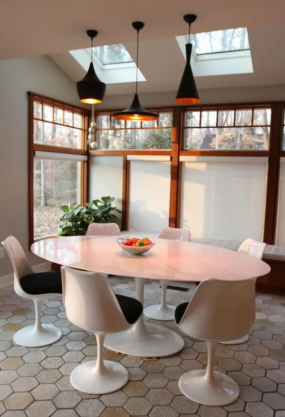 a catchy sunroom with skylights and large windows, an oval table, black Tulip chairs, black pendant lamps and a potted plant