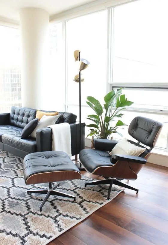 a chic mid-century modern living room with a black leather sofa and an Eames lounger and ottoman, a printed rug, a potted plant