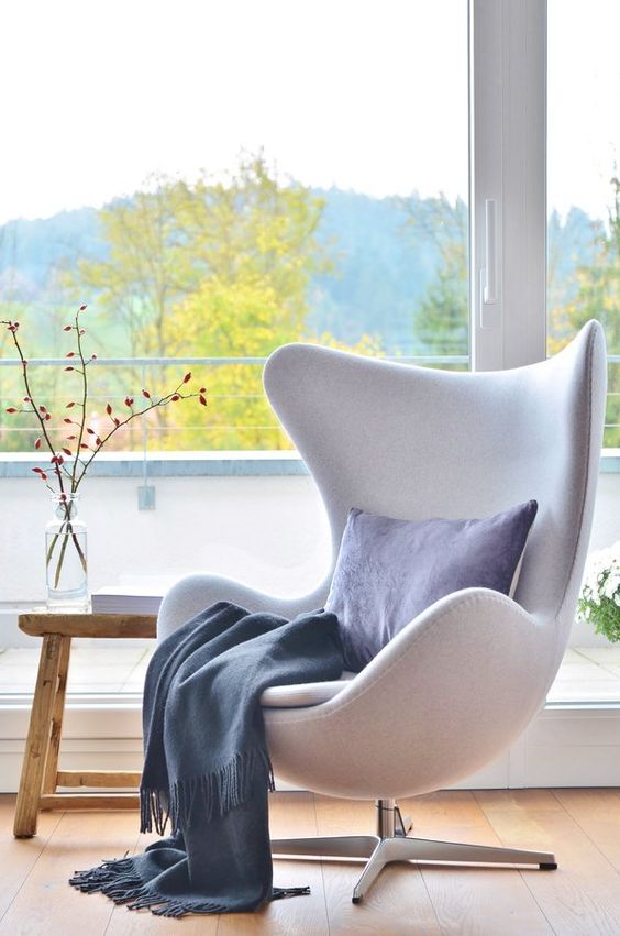 a chic nook with a white Egg chair by the window, a wooden bench and some blue textiles is a lovely space