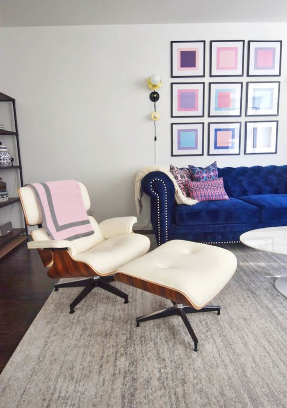 a colorful living room with a bold blue sofa, a creamy Eames lounger, a coffee table and a bright gallery wall