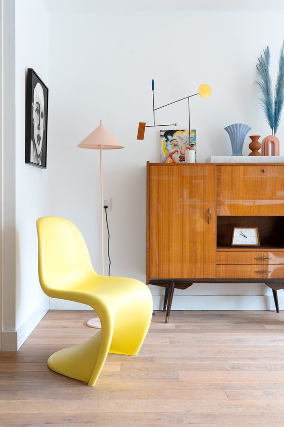 a colorful space with a yellow Pantone chair, a stained credenza, some decor and some lamps is wow