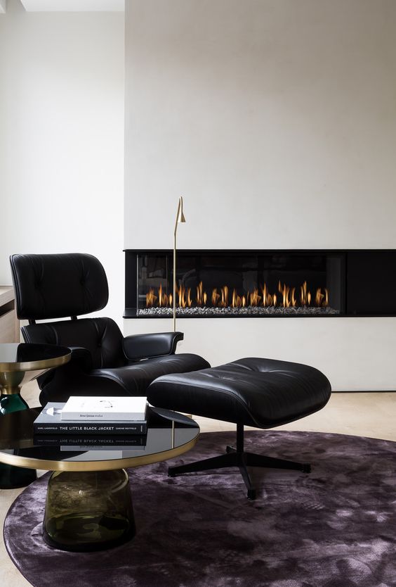 a contemporary space with a built-in ethanol fireplace, a black Eames lounger, a couple of coffee tables and a purple rug