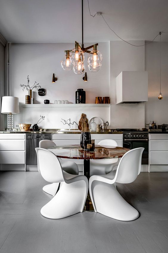 a contemporary white kitchen with sleek cabinets, an open shelf, built-in appliances, a table and white Panton chairs