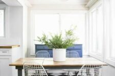 a contrasting dining space by the window, with a blue sideboard, a rustic table, white Eames wire chairs and some greenery