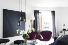 a contrasting living room with a black artwork, purple Swan chairs, bottle pendant lamps, a glass coffee table and a grey sofa