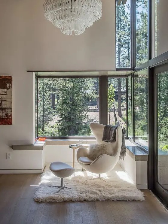 a cool glazed space to enjoy the sun, with a creamy Egg chair and a footrest, a windowsill and a large chandelier