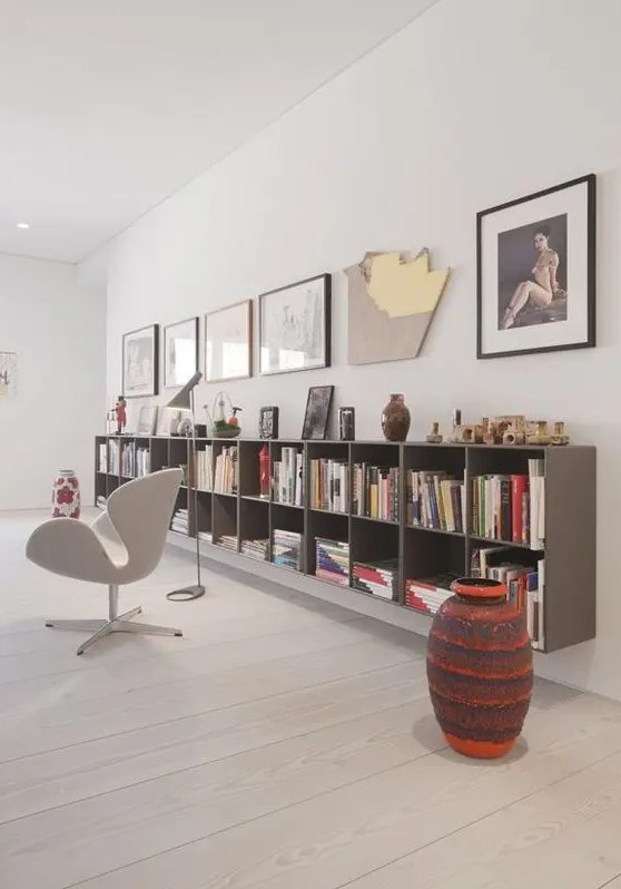 a cool reading space with a grey floating bookcase, a gallery wall, a white Swan chair, a bold side table is cool