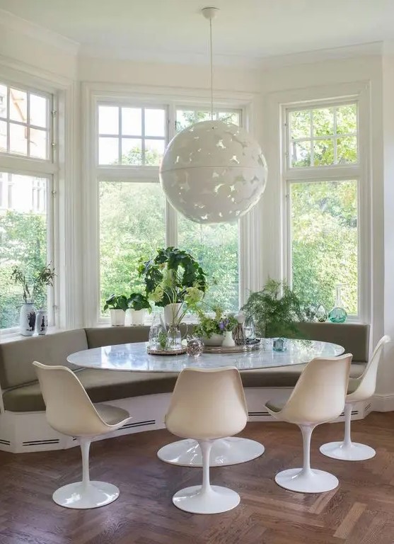 a cozy mid-century modern breakfast nook with a built-in windowsill bench, an oval table, olive green Tulip chairs, a pendant lamp