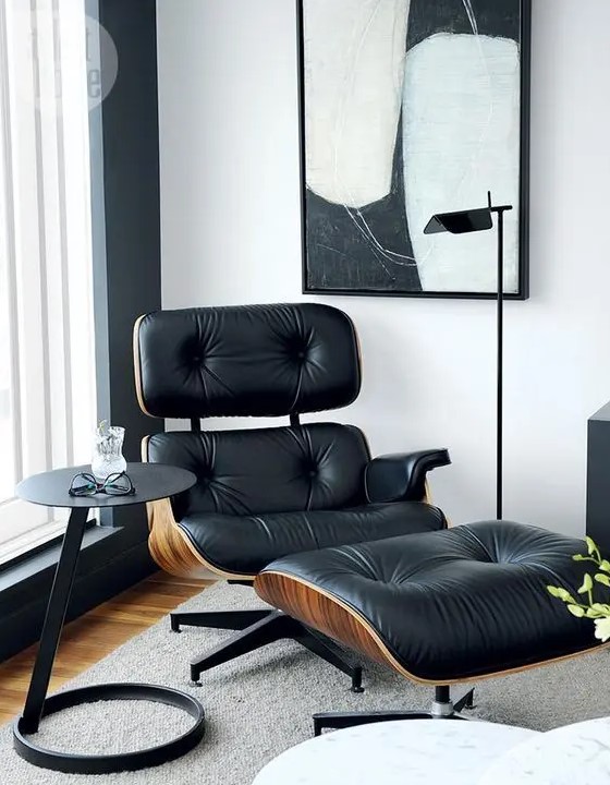 a dramatic nook with a black Eames lounger and ottoman, a side table, a chic floor lamp and a black and white artwork