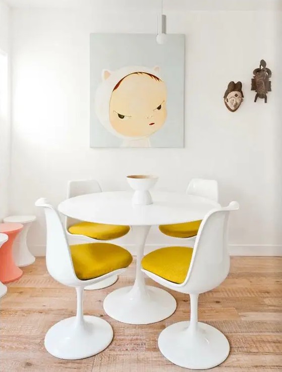 a fun dining space with a round table, mustard Tulip chairs, a fun artwork and Asian decor on the wall, colorful stools
