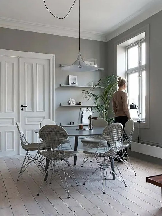 a grey Scandinavian dining space with open shelves, a round dining table, white Eames wire chairs with seat pads, a pendant lamp
