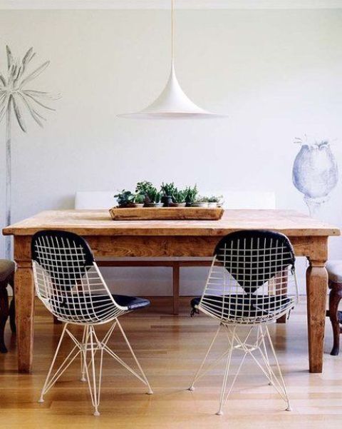 a lovely dining space with a stained table, white Eames wire chairs with black cushions and a white pendant lamp plus greenery